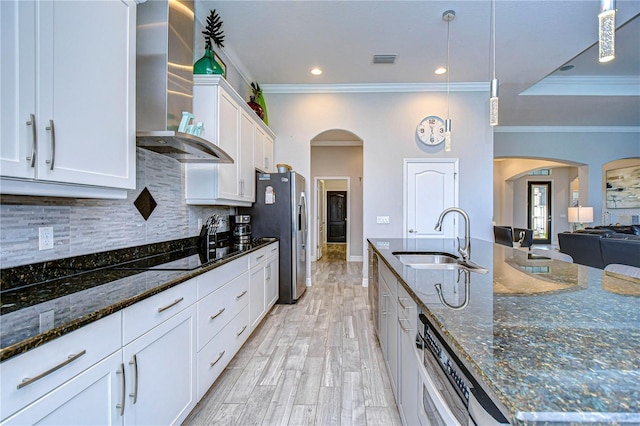 kitchen with dark stone counters, stainless steel appliances, wall chimney range hood, decorative light fixtures, and white cabinetry