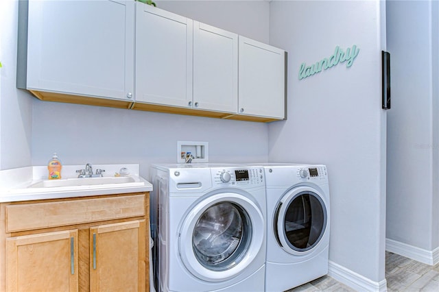 laundry room with cabinets, light wood-type flooring, washing machine and dryer, and sink