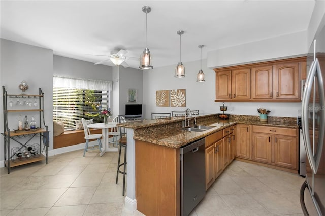 kitchen with sink, dark stone countertops, appliances with stainless steel finishes, a kitchen bar, and kitchen peninsula