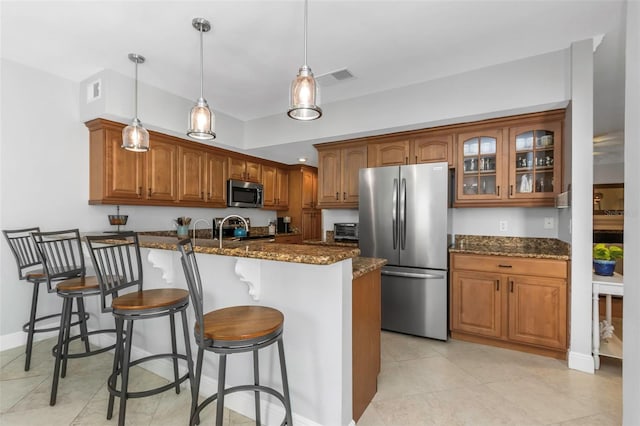 kitchen featuring appliances with stainless steel finishes, pendant lighting, dark stone counters, and a breakfast bar area