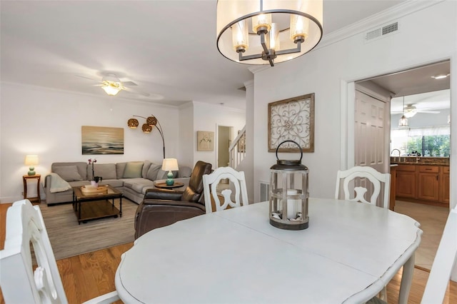 dining area with crown molding, light hardwood / wood-style flooring, and ceiling fan with notable chandelier