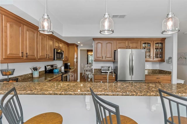 kitchen with a kitchen breakfast bar, dark stone countertops, stainless steel appliances, and decorative light fixtures