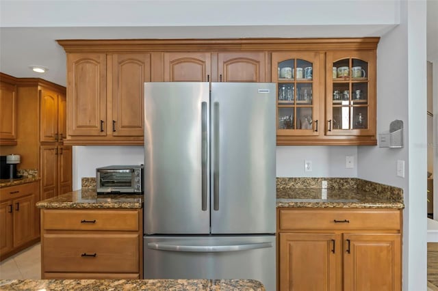 kitchen featuring dark stone countertops, light tile patterned floors, and stainless steel refrigerator