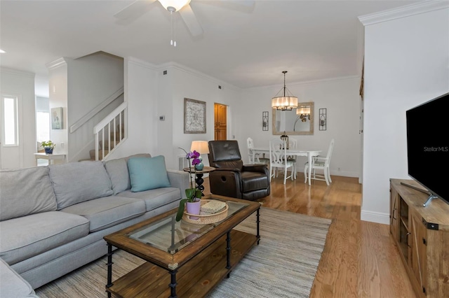 living room featuring ornamental molding, ceiling fan with notable chandelier, and light wood-type flooring