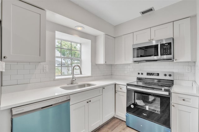 kitchen with appliances with stainless steel finishes, backsplash, sink, white cabinets, and light hardwood / wood-style floors