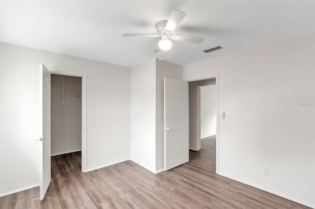 unfurnished bedroom featuring a spacious closet, a closet, ceiling fan, and hardwood / wood-style flooring