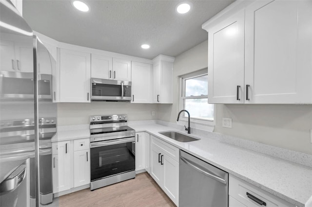 kitchen featuring light stone countertops, a textured ceiling, stainless steel appliances, sink, and white cabinets