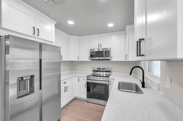 kitchen with light stone countertops, appliances with stainless steel finishes, sink, light hardwood / wood-style flooring, and white cabinets