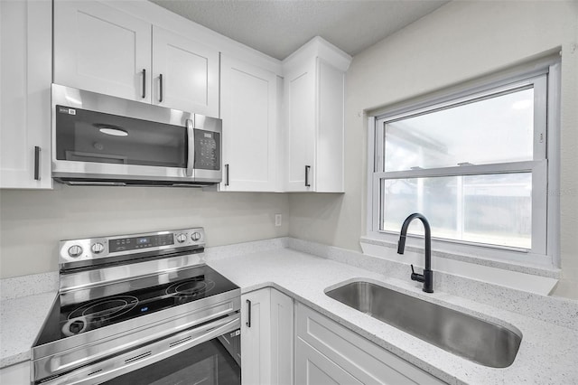 kitchen with light stone countertops, sink, white cabinets, and appliances with stainless steel finishes