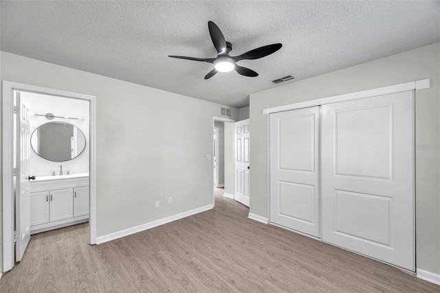 unfurnished bedroom with a textured ceiling, ceiling fan, connected bathroom, light hardwood / wood-style floors, and a closet