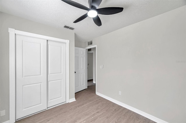 unfurnished bedroom with ceiling fan, light wood-type flooring, a textured ceiling, and a closet