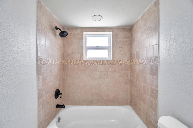 bathroom featuring toilet and tiled shower / bath