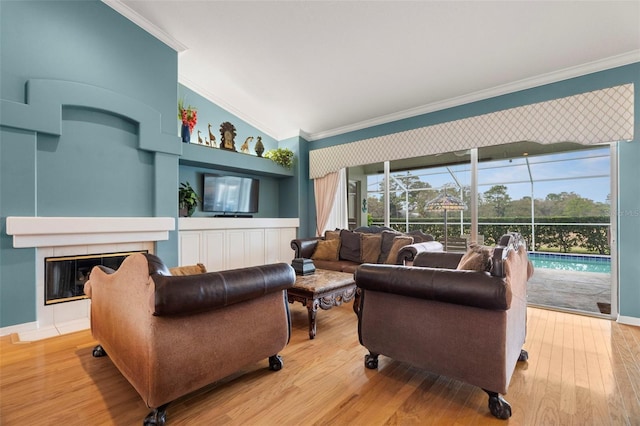 living room with ornamental molding, light wood-type flooring, lofted ceiling, and a tiled fireplace