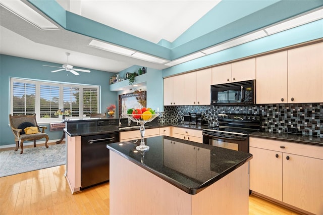 kitchen with kitchen peninsula, light wood-type flooring, dark stone counters, black appliances, and a center island