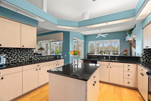 kitchen featuring sink, backsplash, dark stone countertops, a kitchen island, and light wood-type flooring