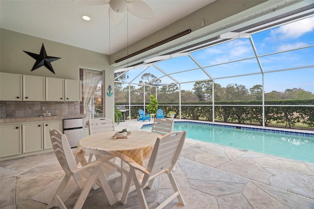 view of swimming pool featuring glass enclosure, ceiling fan, a patio area, and exterior kitchen