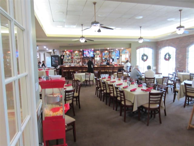 carpeted dining space featuring indoor bar, a tray ceiling, and ceiling fan