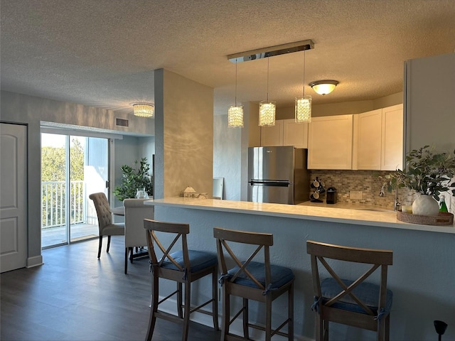 kitchen with stainless steel refrigerator, a breakfast bar area, white cabinets, hanging light fixtures, and kitchen peninsula