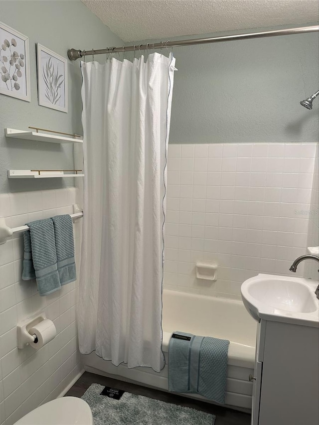 full bathroom with shower / bathtub combination with curtain, tile walls, vanity, a textured ceiling, and toilet