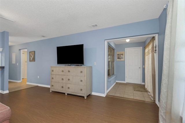 unfurnished living room with baseboards, wood finished floors, visible vents, and a textured ceiling