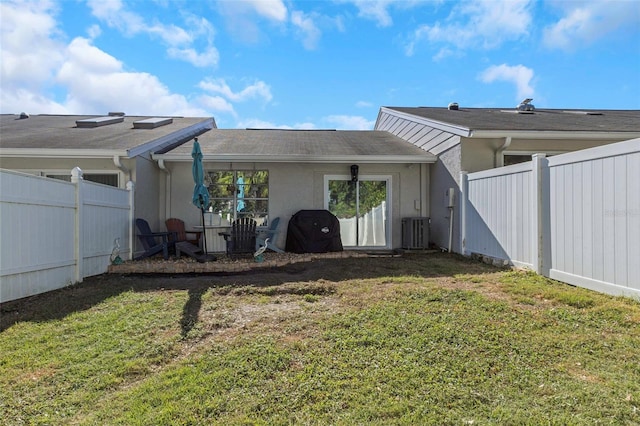 rear view of house with a yard, central AC unit, stucco siding, and fence