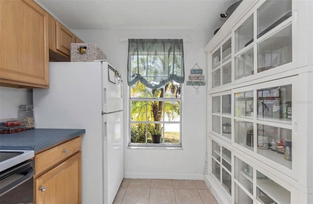 kitchen featuring light tile patterned floors, freestanding refrigerator, electric stove, glass insert cabinets, and dark countertops