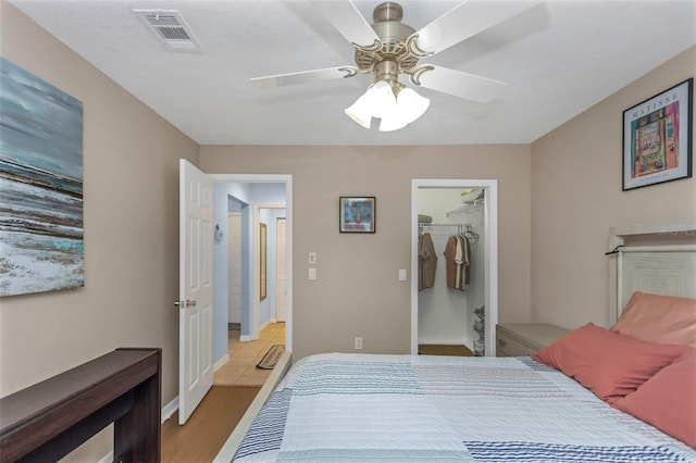 bedroom with wood finished floors, visible vents, ceiling fan, a closet, and a walk in closet