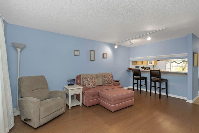 living room featuring baseboards, a textured ceiling, wood finished floors, and track lighting