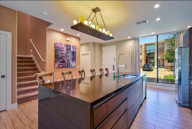 kitchen featuring sink, decorative light fixtures, light wood-type flooring, a large island, and stainless steel refrigerator