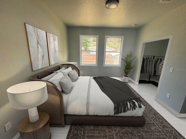 bedroom with visible vents, baseboards, a walk in closet, a textured ceiling, and light wood-type flooring