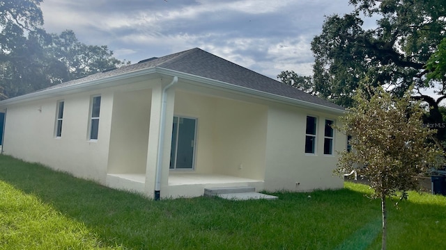 view of side of property with roof with shingles, a lawn, a patio, and stucco siding