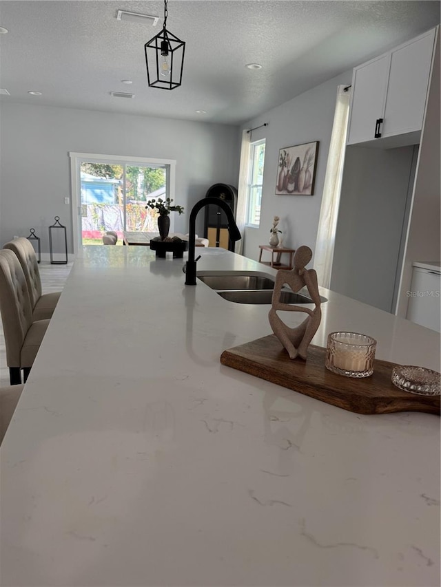 kitchen with white cabinets, open floor plan, light stone countertops, a textured ceiling, and a sink