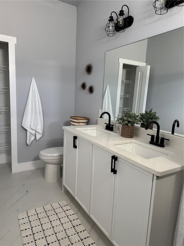 full bathroom with toilet, double vanity, baseboards, and a sink