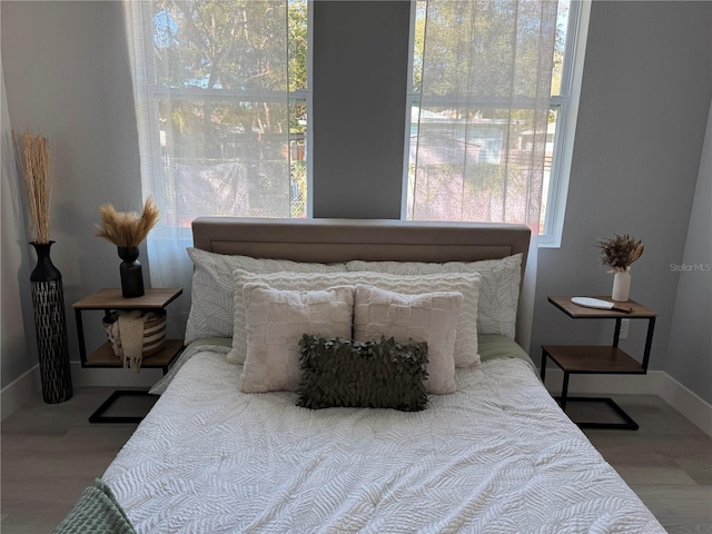 bedroom with multiple windows, baseboards, and wood finished floors