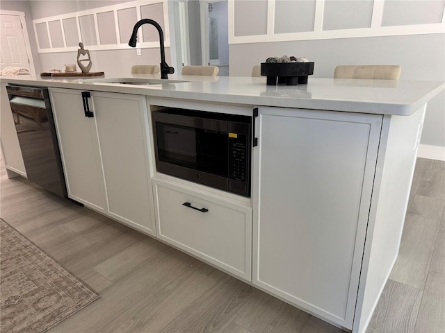 kitchen featuring light wood finished floors, black dishwasher, light countertops, white cabinetry, and a sink