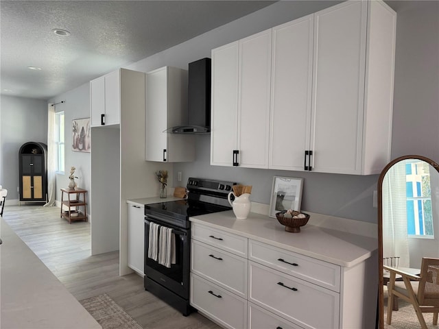 kitchen featuring black / electric stove, white cabinets, light countertops, wall chimney range hood, and light wood finished floors