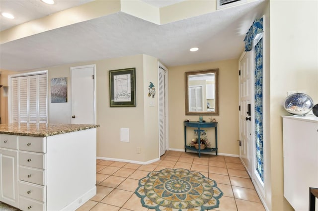 kitchen with a textured ceiling, white cabinetry, light tile patterned floors, and stone countertops