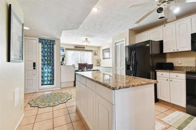 kitchen with stone counters, a kitchen island, light tile patterned flooring, white cabinets, and black appliances