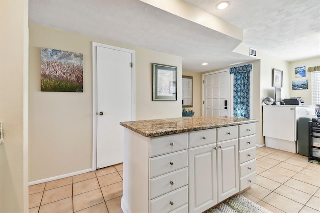 kitchen featuring light stone countertops, light tile patterned floors, white cabinetry, and a kitchen island