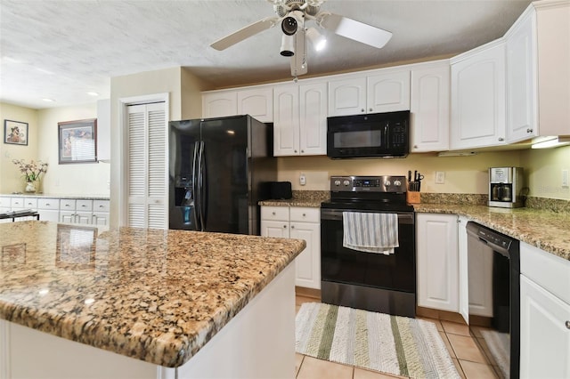 kitchen featuring black appliances, light stone counters, light tile patterned floors, and white cabinets