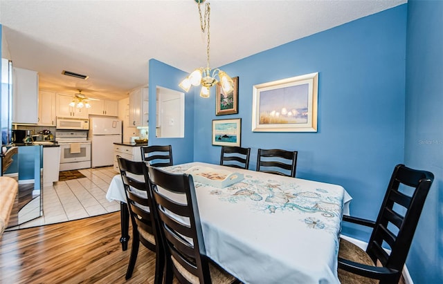 dining area with ceiling fan with notable chandelier and light wood-type flooring