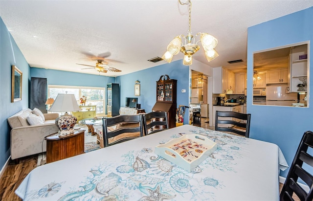 dining room with hardwood / wood-style floors, ceiling fan with notable chandelier, and a textured ceiling