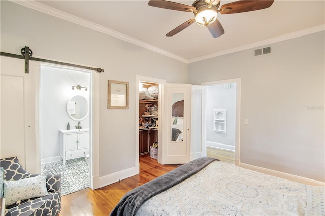 bedroom featuring connected bathroom, a spacious closet, ceiling fan, a barn door, and light hardwood / wood-style flooring