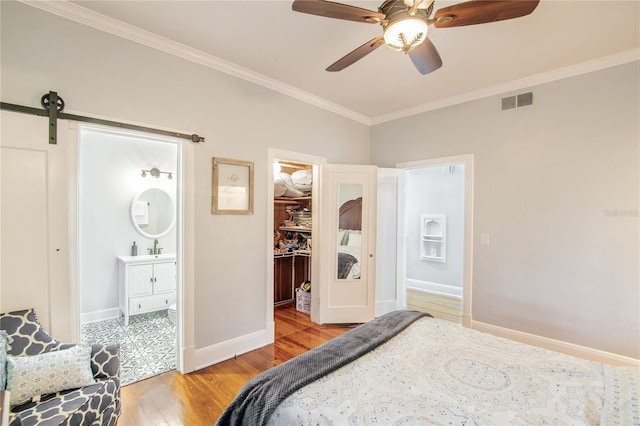 bedroom with a spacious closet, ornamental molding, visible vents, a barn door, and light wood finished floors