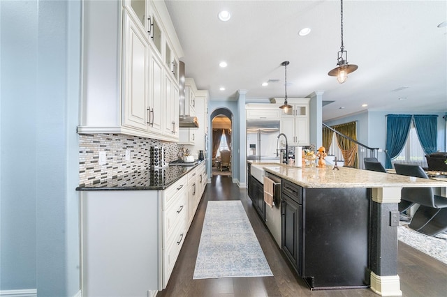 kitchen with white cabinets, backsplash, dark stone counters, hanging light fixtures, and a spacious island