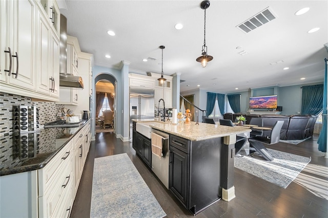 kitchen with dark stone countertops, hanging light fixtures, stainless steel appliances, tasteful backsplash, and an island with sink