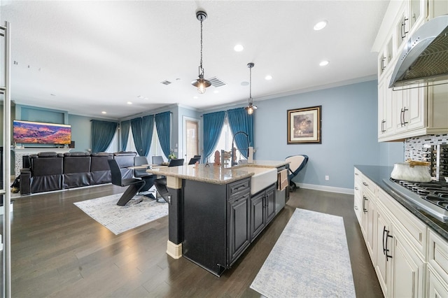 kitchen with crown molding, sink, decorative light fixtures, and a center island with sink