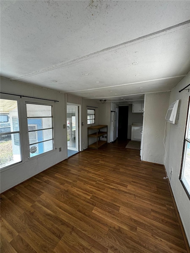 unfurnished living room featuring a textured ceiling, dark wood-type flooring, and a wall unit AC