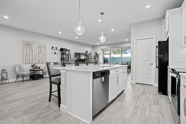 kitchen featuring pendant lighting, a center island with sink, light hardwood / wood-style floors, white cabinetry, and stainless steel appliances