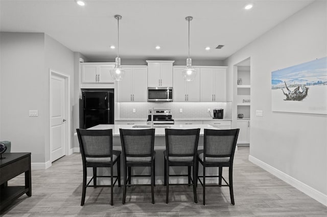 kitchen with white cabinets, stainless steel appliances, hanging light fixtures, and a center island with sink